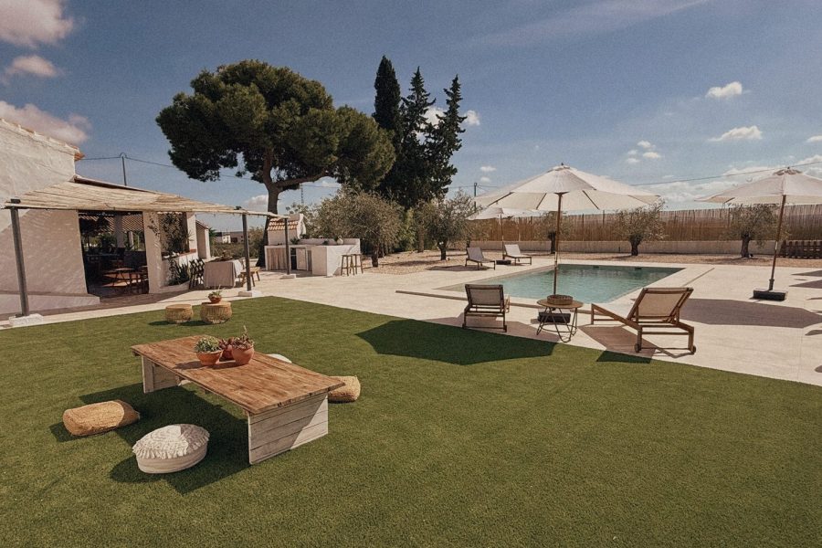Zona de césped con mesa baja y piscina al fondo