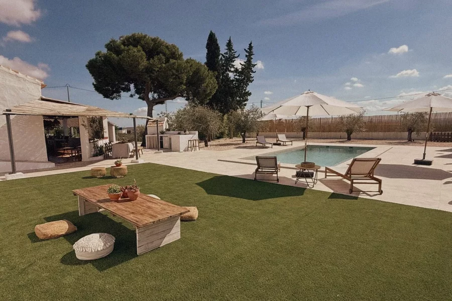 Zona de césped con mesa baja y piscina al fondo